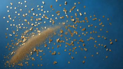 The primary subject of the image is a dusty, golden substance, possibly a powder or a fine sand, that is being blown or scattered across a blue surface. The setting appears to be a room with a blue wall, and the visual style is a close-up of the powdery substance. The colors in the image are predominantly blue and gold, creating a warm and inviting atmosphere.