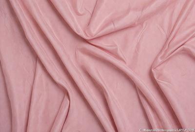 The primary subject of the image is a pink fabric, which is the main object, scene, or focus of the image. The setting or background is a white surface, and the visual style is a close-up of the pink fabric. The colors and mood of the image are predominantly pink, creating a warm and inviting atmosphere.