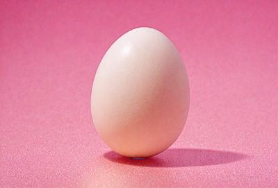 The primary subject of the image is a white egg. The egg is sitting on a pink surface, which could be a table or a counter. The visual style of the image is a photo, capturing the egg in its natural setting. The colors and mood of the image are predominantly pink, giving it a warm and inviting atmosphere.