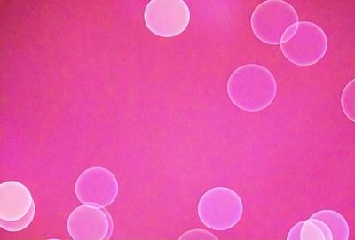 The primary subject of the image is a pink background with a pattern of circles. The circles are of various sizes and are scattered across the background. The setting appears to be a pink room, and the visual style is a combination of a photo and a pattern. The dominant colors in the image are pink and white, creating a warm and inviting atmosphere.