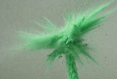 The primary subject of the image is a green, splashing, and spraying substance, which appears to be a green paint or a green dye. The setting is a white background, which provides a clean and uncluttered environment for the green substance to be the main focus. The visual style of the image is a close-up of the green substance, showcasing its vibrant color and texture. The colors and mood of the image are predominantly green, creating a lively and ener