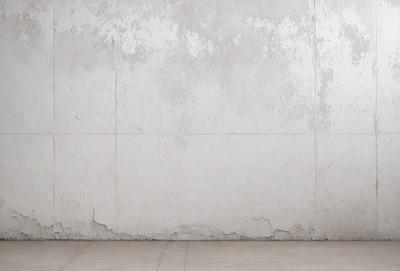The primary subject of the image is a white wall with a peeling paint surface. The setting is a room with a concrete floor. The visual style is a photo, and the colors and mood are predominantly white, giving the image a somewhat dull and aged appearance.
