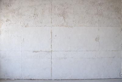 The primary subject of the image is a white wall with a few small holes in it. The setting is a concrete wall, and the visual style is a photo. The dominant colors are white and grey, creating a clean and minimalist atmosphere.