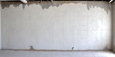 The primary subject of the image is a large, empty white wall. The setting is a room with a concrete floor. The visual style is a photo, and the colors and mood are predominantly white, giving the scene a clean and minimalist appearance.