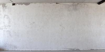 The primary subject of the image is a large, white wall with a peeling paint surface. The setting is an indoor environment, possibly a room or a building. The visual style of the image is a photo, capturing the peeling paint and the overall atmosphere of the wall. The colors in the image are predominantly white, with the peeling paint adding a touch of brown and grey. The mood of the image is somewhat dull and aged, reflecting the condition of the wall.