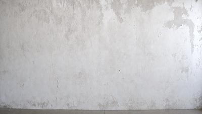 The primary subject of the image is a white wall with a rough texture. The setting is a room with a concrete wall, and the visual style is a photo. The colors and mood of the image are predominantly white, giving it a clean and minimalist appearance.