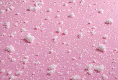 The primary subject of the image is a pink surface with white powder or sugar sprinkled on it. The setting appears to be a room with a pink background. The visual style is a close-up of the pink surface with the white powder, creating a textured and visually appealing scene. The colors and mood of the image are predominantly pink and white, giving it a warm and inviting atmosphere.