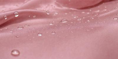 The primary subject of the image is a piece of pink fabric with water droplets on it. The setting is a pink background, and the visual style appears to be a photo. The colors in the image are predominantly pink, and the overall atmosphere is wet and slightly shiny.