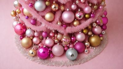 The primary subject of the image is a pink and white Christmas tree decorated with various ornaments. The tree is adorned with pink and white ornaments, including pink and white balls, and gold ornaments. The setting is a pink background, which adds a festive touch to the scene. The visual style of the image is a combination of photo and digital art, creating a unique and eye-catching display. The colors and mood of the image are predominantly pink and white, giving it a