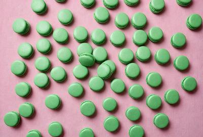 The primary subject of the image is a close-up of a green macaron, which is the main object in the scene. The setting is a pink background, and the visual style is a photo. The dominant colors are green and pink, creating a lively and appetizing atmosphere.