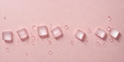 The primary subject of the image is a close-up of four small, clear, and wet glass squares. The setting is a pink surface, which adds a warm and inviting atmosphere to the scene. The visual style is a close-up, which emphasizes the details of the glass squares. The colors and mood of the image are predominantly pink, creating a sense of warmth and softness.