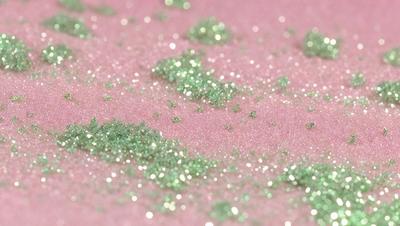 The primary subject of the image is a close-up of a pink surface with glittery green specks on it. The setting appears to be a pink background, and the visual style is a close-up of the pink surface with the green specks. The colors and mood of the image are predominantly pink and green, creating a visually appealing and vibrant scene.