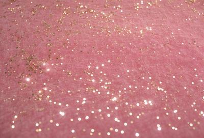 The primary subject of the image is a close-up of a pink fabric with gold glitter sprinkled on it. The setting is a pink background, and the visual style appears to be a photo. The colors and mood of the image are predominantly pink and gold, creating a warm and inviting atmosphere.