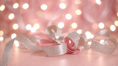The primary subject of the image is a pink ribbon with silver glitter on it. The ribbon is placed on a pink surface, which adds to the overall color scheme of the image. The visual style of the image is a close-up of the ribbon, showcasing its details and texture. The colors and mood of the image are predominantly pink and warm, creating a sense of femininity and elegance.