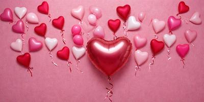 The primary subject of the image is a heart-shaped balloon, which is the main focus of the scene. The balloon is pink and is placed on a pink background, creating a warm and romantic atmosphere. The visual style of the image is a close-up of the heart balloon, emphasizing its shape and color.