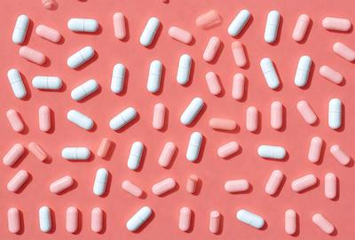 The primary subject of the image is a large number of pills arranged in a pattern on a pink surface. The setting is a pink background, and the visual style appears to be a pattern or a collage of pills. The colors and mood of the image are predominantly pink, giving it a warm and inviting atmosphere.