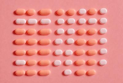 The primary subject of the image is a collection of pills, which are arranged in a pattern on a pink surface. The setting is a pink background, and the visual style appears to be a close-up of the pills. The colors and mood of the image are predominantly pink, giving it a warm and inviting atmosphere.