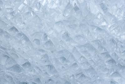 The primary subject of the image is a large, white, frosty surface with a pattern of small, clear, shiny, and reflective pieces. The setting is a snowy environment, and the visual style appears to be a combination of a photo and digital art. The colors and mood of the image are predominantly white and cold, creating a sense of winter and frost.