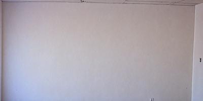 The image features a large, empty white wall with no visible objects or decorations. The wall appears to be a canvas, ready for artistic expression. The primary subject is the white wall, which serves as the main focus of the image. The setting is a plain, unadorned space, and the visual style is a simple, uncluttered presentation. The colors and mood of the image are predominantly white, creating a clean and minimalist atmosphere.