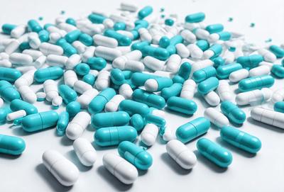 The primary subject of the image is a pile of blue and white pills. The pills are scattered across a white surface, creating a visually appealing and colorful display. The setting appears to be a clean and organized environment, possibly a pharmacy or a medical facility. The visual style of the image is a close-up of the pills, emphasizing their vibrant colors and unique shapes. The overall atmosphere of the image is one of cleanliness and organization, with the pills being the main focus of