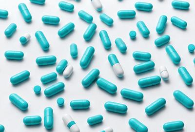 The primary subject of the image is a large number of blue pills arranged in a pattern. The setting is a white background, which provides a clean and uncluttered appearance. The visual style is a close-up of the pills, showcasing their vibrant blue color. The overall atmosphere is one of organization and attention to detail, as the pills are neatly arranged in a visually appealing manner.