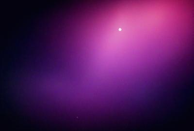 The primary subject of the image is a purple sky with a moon visible in the background. The setting is a nighttime scene with a pinkish hue. The visual style is a combination of a photo and digital art, creating a unique and artistic atmosphere. The colors and mood of the image are predominantly purple and pink, giving it a serene and dreamy quality.
