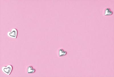 The primary subject of the image is a pink background with three silver heart-shaped decorations. The setting is a pink wall, and the visual style is a close-up of the heart decorations. The colors and mood of the image are predominantly pink, creating a warm and inviting atmosphere.