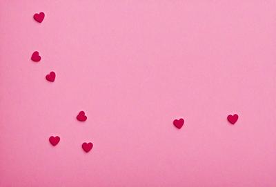 The primary subject of the image is a pink background with a row of red hearts attached to it. The hearts are arranged in a straight line, creating a visually appealing pattern. The setting appears to be a pink wall, which serves as the background for the hearts. The visual style of the image is a combination of a photo and digital art, as the hearts are digitally placed on the pink wall. The colors and mood of the image are predominantly pink and warm, giving it a cozy and inv