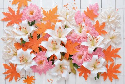 The primary subject of the image is a beautiful arrangement of white and pink flowers, including lilies, placed on a white surface. The flowers are scattered across the surface, creating a visually appealing and colorful display. The setting appears to be a table or a similar surface, providing a clean and uncluttered backdrop for the flowers. The visual style of the image is a combination of realistic and artistic elements, as the flowers are depicted in a way that showcases their beauty and natural form. The colors