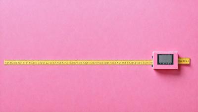 The primary subject of the image is a ruler, which is placed on a pink surface. The ruler is long and has a yellow line on it. The setting is a pink background, which creates a contrast with the yellow line on the ruler. The visual style of the image is a close-up of the ruler, emphasizing its details. The colors and mood of the image are predominantly pink, giving it a warm and inviting atmosphere.