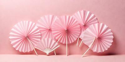 The primary subject of the image is a group of five pink and white umbrellas. They are arranged in a row, with each umbrella having a different design. The setting is a pink background, which creates a visually appealing contrast with the umbrellas. The visual style of the image is a combination of photo and digital art, as it appears to be a photograph of a digital artwork. The colors and mood of the image are predominantly pink and white, giving it a cheerful