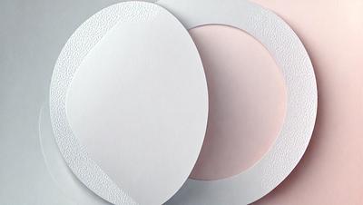 The image features a set of four white, round, and decorative paper plates. The plates are arranged in a circular pattern, with each plate slightly overlapping the others. The plates are placed on a pink surface, which adds a touch of color to the scene. The overall atmosphere of the image is elegant and inviting, with the decorative paper plates serving as a focal point.