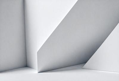 The primary subject of the image is a white paper with a triangular shape. The paper is placed on a white surface, which creates a clean and minimalist visual style. The setting appears to be a simple, uncluttered environment, with no other objects or distractions visible in the image. The colors and mood of the image are predominantly white, giving it a calm and serene atmosphere.