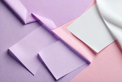 The primary subject of the image is a stack of paper, which is purple and pink in color. The setting is a table, and the visual style appears to be a photo. The colors and mood of the image are predominantly purple and pink, creating a warm and inviting atmosphere.
