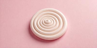 The primary subject of the image is a white, round, and swirly object, which appears to be a piece of cake or a pastry. The setting is a pink surface, which adds a contrasting and vibrant touch to the scene. The visual style of the image is a close-up, focusing on the intricate details of the swirly object. The colors and mood of the image are predominantly pink and white, creating a sense of warmth and elegance.