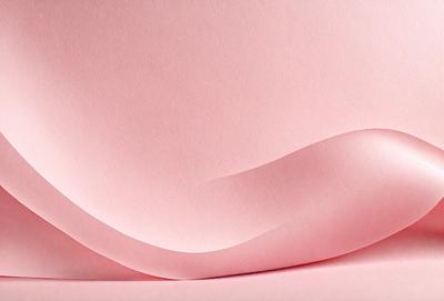 The primary subject of the image is a large piece of pink paper. The setting is a table, and the visual style is a close-up of the paper. The colors and mood of the image are predominantly pink, creating a warm and inviting atmosphere.