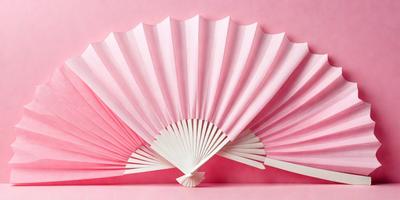 The primary subject of the image is a white fan with pink and white paper. The fan is open and appears to be made of paper. The setting is a pink background, which adds a vibrant and warm atmosphere to the scene. The visual style is a combination of a photo and a drawing, as the fan is a real object, but the paper is drawn or illustrated. The colors and mood of the image are predominantly pink and white, creating a sense of elegance and simplicity.
