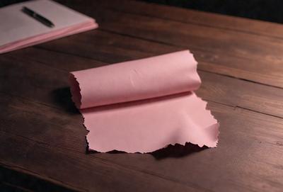 The primary subject of the image is a pink sheet of paper. The setting is a wooden table, and the visual style is a photo. The colors and mood of the image are predominantly pink, giving it a warm and inviting atmosphere.