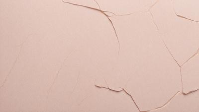 The primary subject of the image is a piece of pink paper with a cracked and peeling surface. The setting is a close-up view of the paper, showcasing the damage and wear. The visual style is a realistic representation of the paper, and the colors are predominantly pink, giving the image a slightly faded and aged appearance.