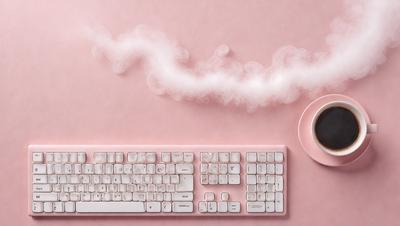 The primary subject of the image is a computer keyboard. The keyboard is placed on a pink surface, which appears to be a table. The setting is a room with a pink background, giving the scene a warm and inviting atmosphere. The visual style of the image is a close-up of the keyboard, emphasizing its details and design. The colors and mood of the image are predominantly pink, creating a sense of comfort and relaxation.