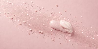 The primary subject of the image is a close-up of a pink surface with a white substance, possibly a cream or a powder, spread across it. The setting appears to be a pink background, which adds to the overall mood of the image. The visual style of the image is a close-up, which emphasizes the details of the white substance on the pink surface. The colors and mood of the image are predominantly pink and soft, creating a sense of warmth and delic