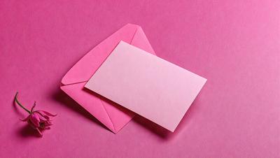 The primary subject of the image is a pink card with a pink envelope. The card is placed inside the envelope, which is sitting on a pink surface. The visual style of the image is a photo, and the colors and mood are predominantly pink, creating a warm and inviting atmosphere.