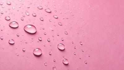 The primary subject of the image is a pink surface with water droplets on it. The setting is a pink background, and the visual style is a close-up of the pink surface with water droplets. The colors and mood of the image are predominantly pink, creating a warm and inviting atmosphere.
