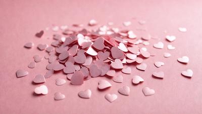 The primary subject of the image is a pile of pink hearts. The hearts are scattered across a pink surface, creating a visually appealing and romantic scene. The setting appears to be a pink background, which complements the hearts' color and adds to the overall mood of the image. The visual style of the image is a close-up of the hearts, emphasizing their details and texture.
