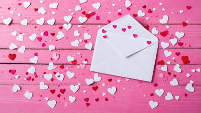 The primary subject of the image is a white envelope with hearts on it, placed on a pink background. The setting appears to be a creative and playful environment, possibly a Valentine's Day or a romantic scene. The visual style of the image is a combination of photo and digital art, as it features a close-up of the envelope with hearts and a pink background. The colors and mood of the image are predominantly pink and heartwarming, evoking feelings of love and affection