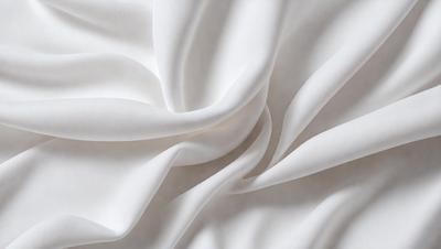 The primary subject of the image is a white sheet of fabric, which is the main object, scene, or focus of the image. The setting is a white background, which provides a clean and minimalistic environment. The visual style is a close-up of the fabric, showcasing its texture and details. The colors and mood of the image are predominantly white, giving it a clean, serene, and elegant appearance.