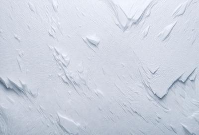 The primary subject of the image is a white wall with a pattern of white and gray swirls. The setting is a room with a white wall, and the visual style is a close-up of the wall. The colors and mood of the image are predominantly white and gray, creating a clean and minimalist atmosphere.