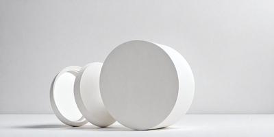 The primary subject of the image is a group of three white, round, flat objects, possibly made of ceramic or plastic, sitting on a white surface. The objects are arranged in a way that they appear to be stacked or placed next to each other. The setting is a white background, which provides a clean and minimalist appearance to the scene. The visual style of the image is a close-up of the objects, emphasizing their shape and texture. The colors and mood of the image are predominantly white,