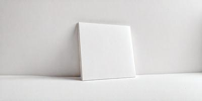 The primary subject of the image is a white cardboard box. The box is placed on a white surface, which could be a table or a wall. The visual style of the image is a photo, capturing the details of the cardboard box. The colors and mood of the image are predominantly white, giving it a clean and minimalist appearance.