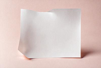 The primary subject of the image is a white piece of paper. The paper is folded in half, creating a creased surface. The setting is a pink background, which adds a warm and inviting atmosphere to the scene. The visual style of the image is a close-up of the paper, showcasing its texture and details. The colors and mood of the image are predominantly white and pink, giving it a clean and gentle appearance.